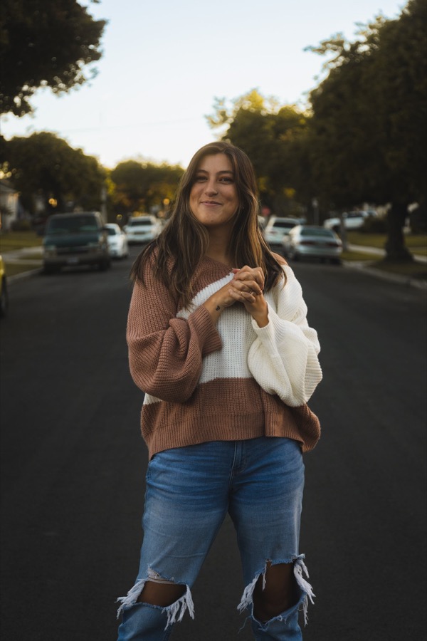 A woman standing in the middle of a tree-lined street in low golden light