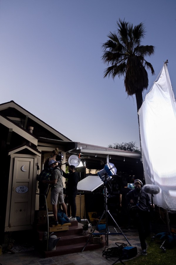 A film set at dusk, lights and diffusion rigged outside a house