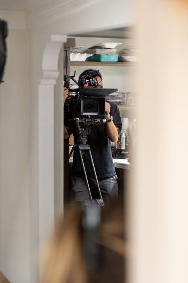 A cinema camera on a tripod framed through a doorway, the operator behind it