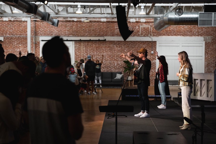 A band playing a low stage in a brick warehouse, the room full of people standing