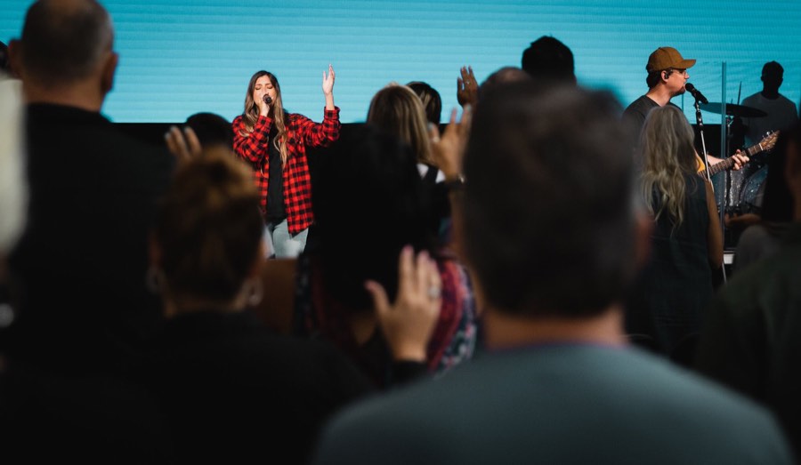 A singer on stage seen over the heads of a standing crowd, hands raised in front of her