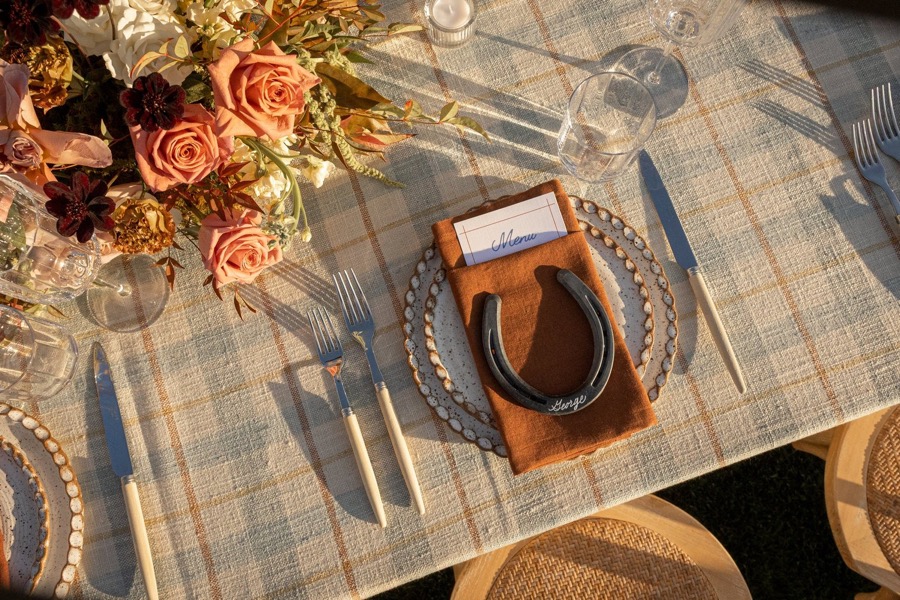 Overhead of a reception table set with roses, glassware and a leather horseshoe