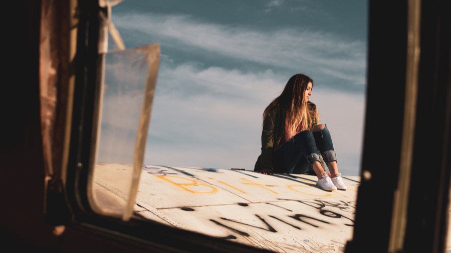 A woman sitting in a weathered window frame with open sky behind her