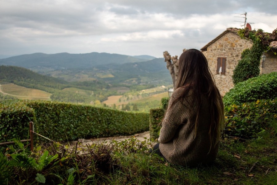 A woman sitting on a garden wall looking out over hills and farmland