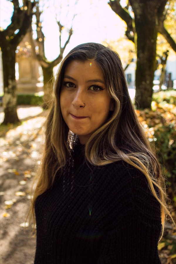 A woman in a black turtleneck backlit under a canopy of bare trees