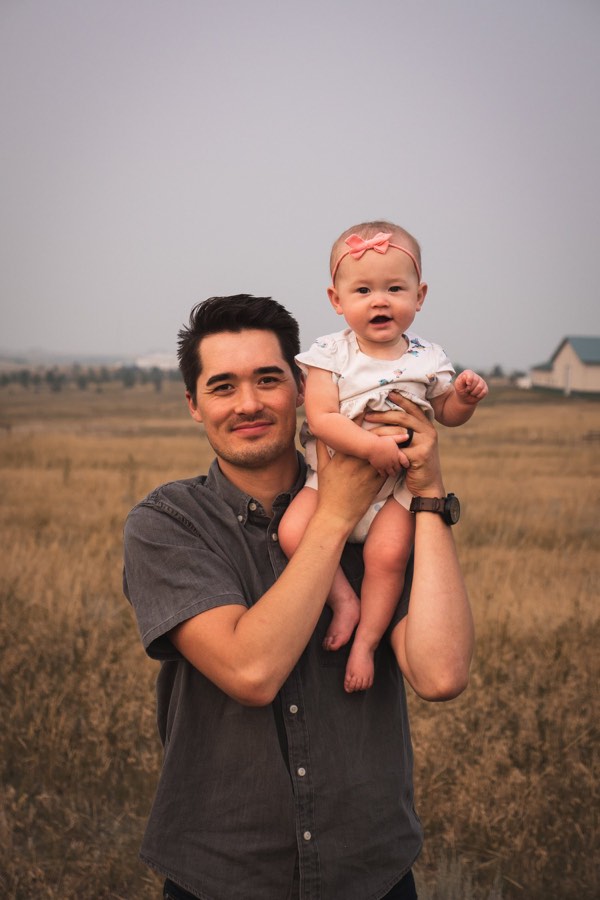 A man holding a baby up in his arms in a field of dry grass
