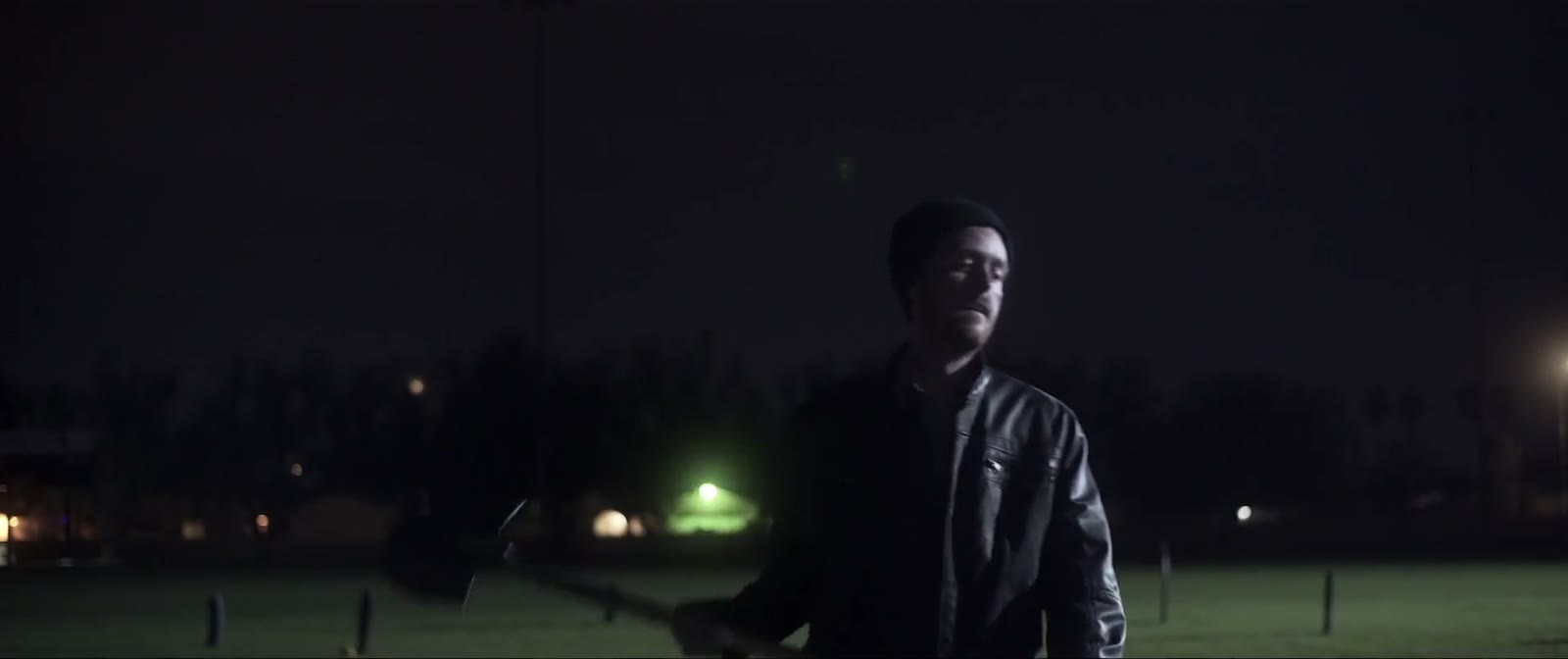 A man alone in a dark field at night with a shovel